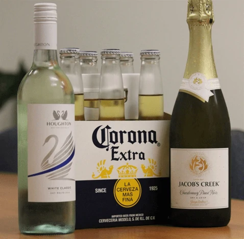 A bottle of Corona Extra alongside two bottles of red wine on a wooden surface.