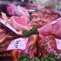 Various cuts of meat are displayed in a store, each with clear labels indicating type and price.